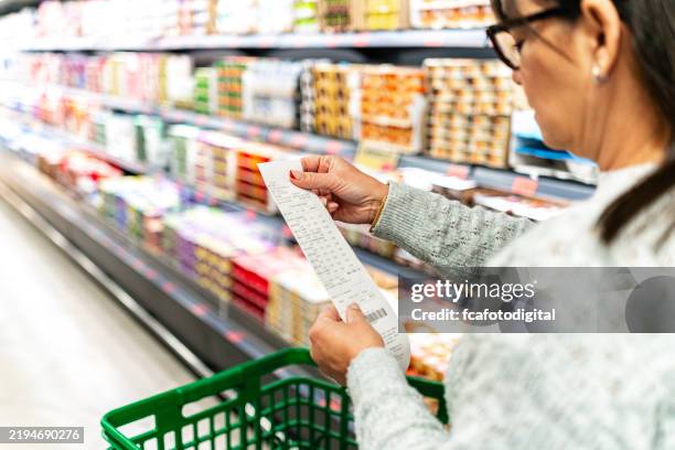 frau kauft im supermarkt ein und prüft ihre quittung - inflation stock-fotos und bilder