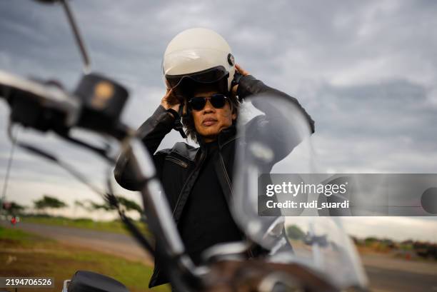 a senior man getting on a motorcycle. - old-man-motorcycle stock pictures, royalty-free photos & images