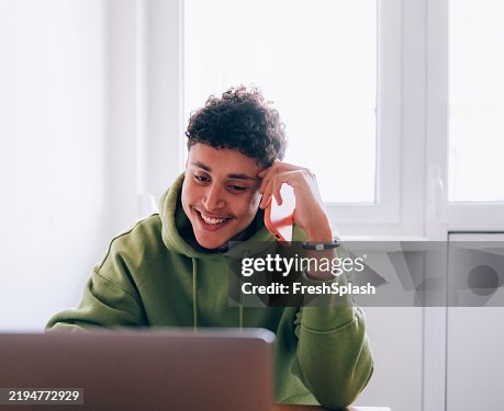 Young Man Smiling While Using Laptop and Talking on a Smartphone Young Man Smiling While Using Laptop and Talking on a Smartphone