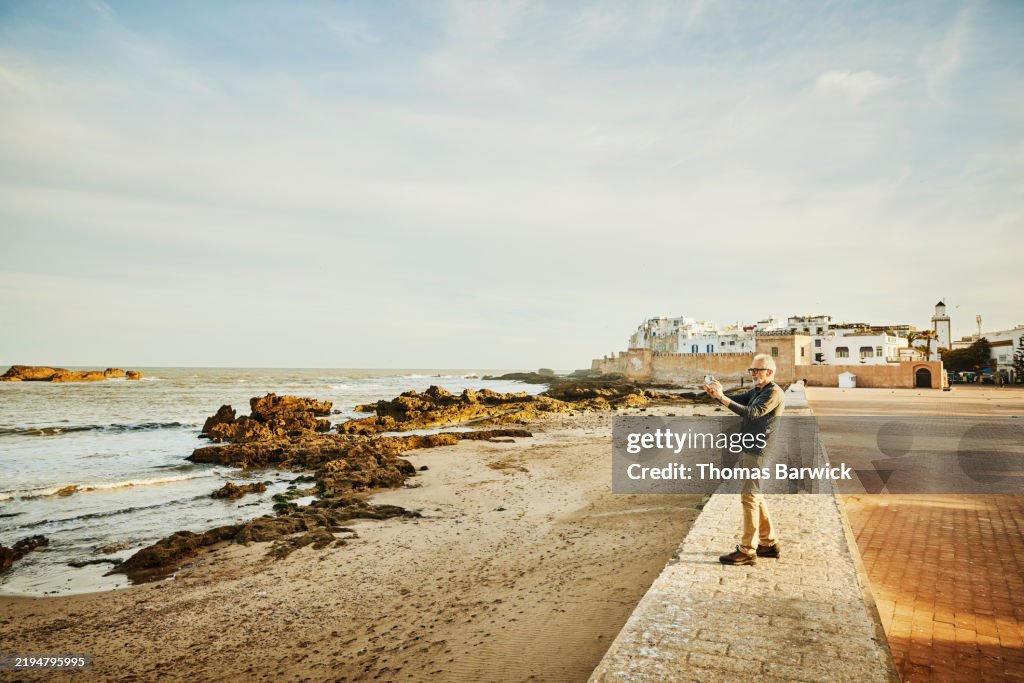 Extreme wide shot senior man taking photos of Essaouira at sunrise