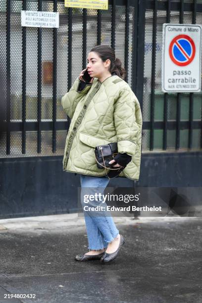 Guest wears dark green oversized puffy padded jacket, light blue straight denim jean pants, shiny black Masion Marigela Tabi flats leather shoes,...