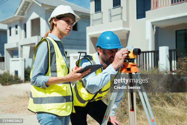 construction workers conducting land survey with theodolite at a housing development site - land surveyor stock pictures, royalty-free photos & images