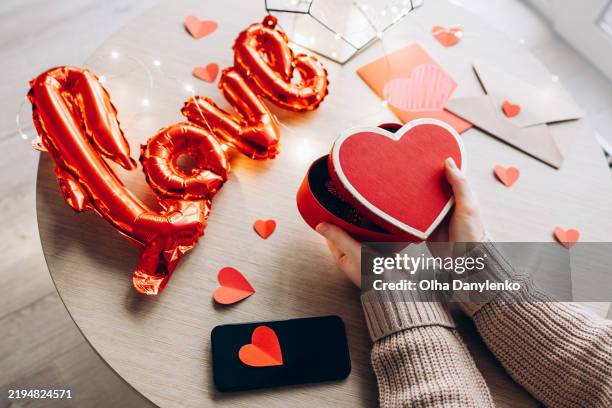 happy valentine's day card. woman opening a heart-shaped gift box on a wooden table with romantic decorations and cozy fairy lights - día de san valentín fotografías e imágenes de stock