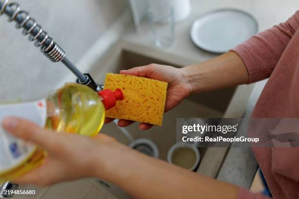 frau, die spülmittel auf einen schwamm gießt, bereitet sich darauf vor, geschirr zu spülen - spülmittel stock-fotos und bilder