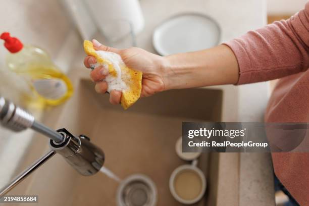 woman squeezing a soapy sponge while washing dishes in the kitchen sink - washing up liquid stock pictures, royalty-free photos & images