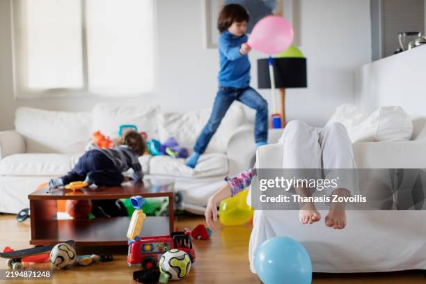 kids jumping on sofas while exhausted mother rests - caos fotografías e imágenes de stock