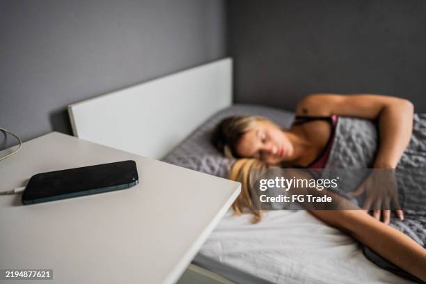 chargement du smartphone et femme dormant en arrière-plan à la maison - chargeur de batterie photos et images de collection