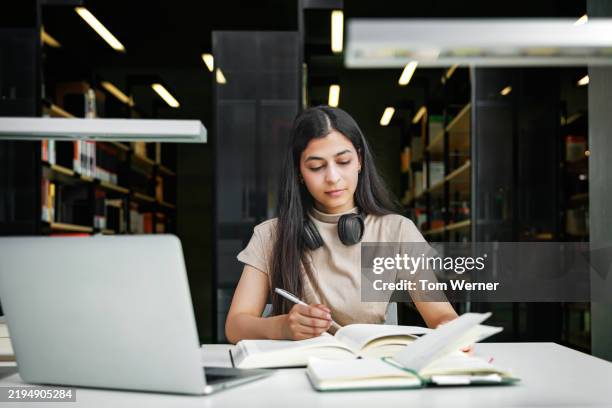 female student studying with books and laptop in library - avaliação imagens e fotografias de stock