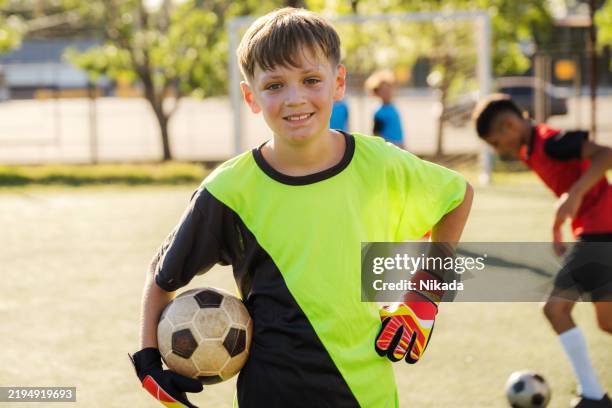 jeune garçon tenant un ballon de football pendant la journée sur un terrain de sport - tenue de football photos et images de collection