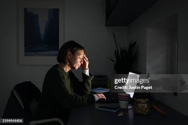 powerful portrait of a mature woman working from home. she looks tired and stressed - overworked - women working from home stock pictures, royalty-free photos & images