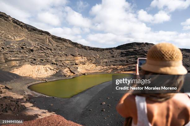 Woman takes a photo of the green lagoon charco Clico in volcanic landscape