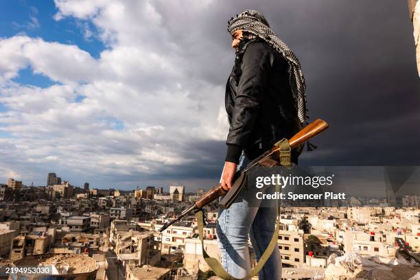 Man poses with a Kalashnikov rifle while standing above the city of Homs on January 20, 2025 in Homs, Syria. Homs, the country’s third-largest city,...