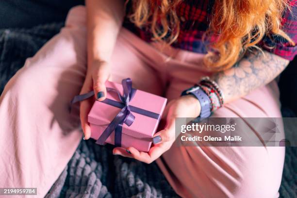 woman holding a wrapped gift box with purple ribbon in cozy setting - generosidad fotografías e imágenes de stock
