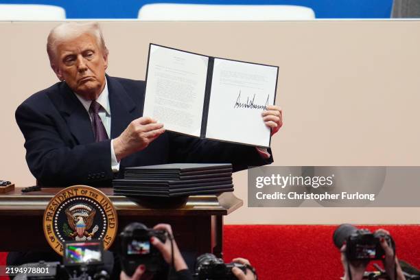 President Donald Trump holds up an executive order after signing it during an indoor inauguration parade at Capital One Arena on January 20, 2025 in...