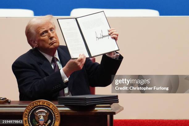 President Donald Trump holds up an executive order after signing it during an indoor inauguration parade at Capital One Arena on January 20, 2025 in...