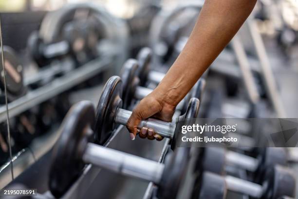 primer plano de una mano levantando una mancuerna en un entorno de gimnasio - equipo de formación fotografías e imágenes de stock