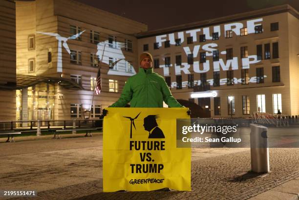 Greenpeace activist holds a banner showing a wind turbine and that reads: "Future vs. Trump" as the same image is projected on the facade of the U.S....
