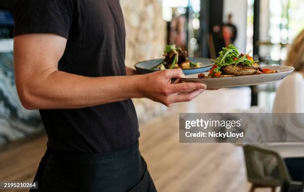 kellner, der den gästen eines restaurants ein gericht serviert - kellnerberuf stock-fotos und bilder
