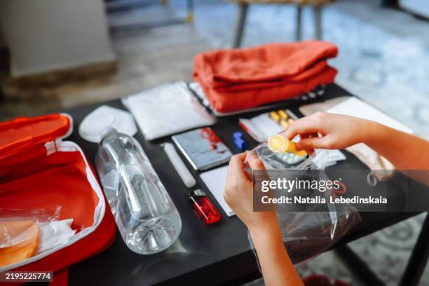 a woman's hands prepare a doomsday kit, packing a flashlight and essential survival items on the table. - cadena alimentaria fotografías e imágenes de stock