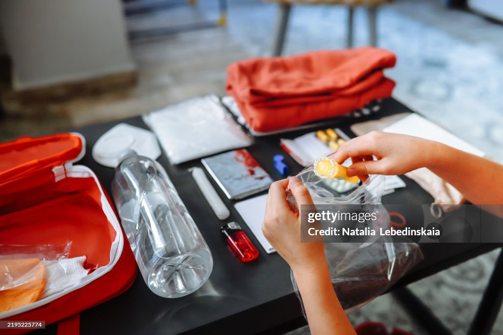A woman's hands prepare a doomsday kit, packing a flashlight and essential survival items on the table.