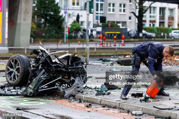 January 2025, Duesseldorf: A police officer secures traces, on the left the torn off front axle of the BMW X5 involved in the accident. Photo:...