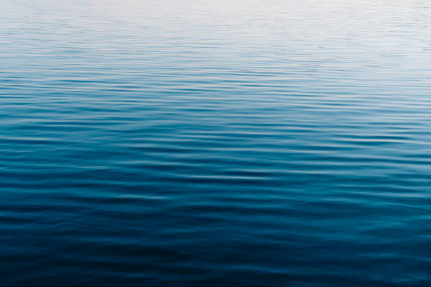 calm blue water of a serene lake reflecting the morning sky - ripple in still water stock pictures, royalty-free photos & images