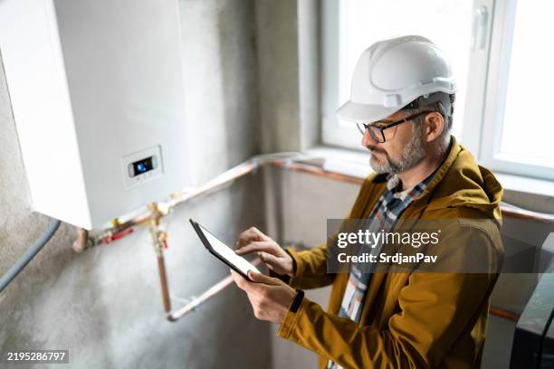 techniker bei der inspektion einer gasheizung mit digitalem tablet in einer modernen umgebung - heizungsmonteur stock-fotos und bilder