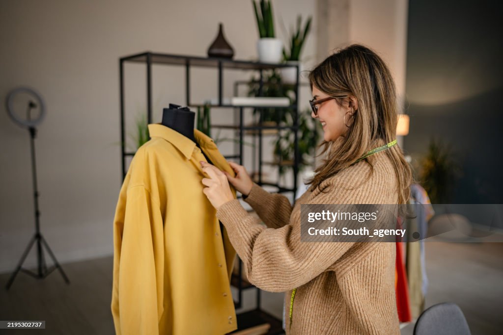 Frau passt gelbe Jacke an einer Schaufensterpuppe in einem modernen Studio-Ambiente mit Pflanzen und kreativem Dekor an