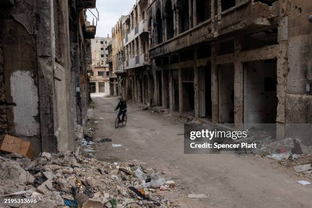 Man rides a bicycle through a neighborhood heavily damaged after years of war in the city of Homs on January 22, 2025 in Homs, Syria. Homs, the...