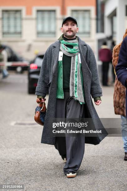 Guest wears a black cap, a white and green scarf, a green and white leather jacket, a dark green pullover, a grey coat, grey wide-leg pants, a blue...