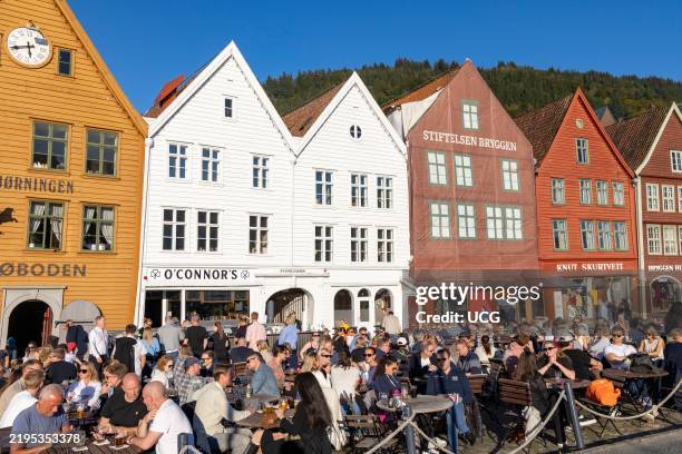Friends and couples enjoy the afternoon autumn sunshine and a drink together outside the bars and pubs in Bryggen district of Bergen.