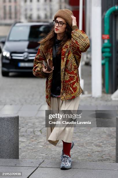 Guest wears black shirt, red and beige printed quilted jacket, beige midi skirt, red socks, grey New Balance sneakers, brown fur hat, outside...