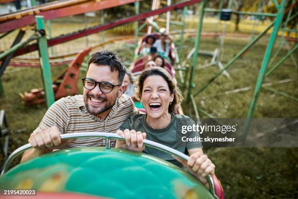 young happy couple having fun on rollercoaster at amusement park. - achtbaan stockfoto's en -beelden