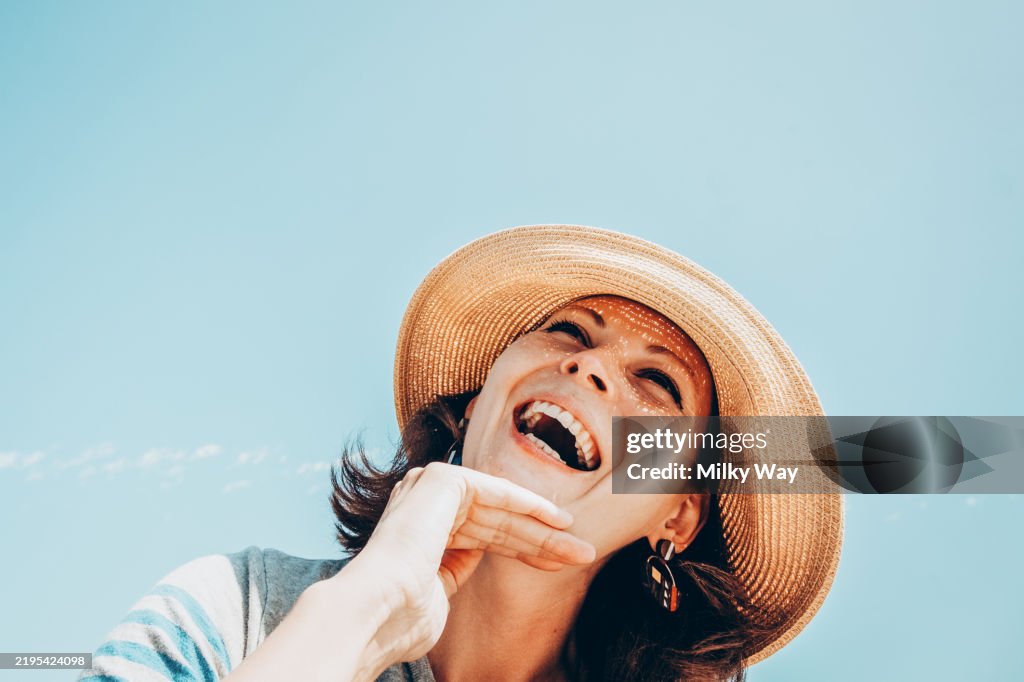 Joyful summer day with smiling woman in sun hat under clear blue sky.
