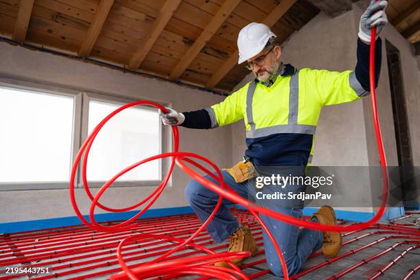 construction worker installing radiant floor heating using red tubing indoors - radiant floor heating stock pictures, royalty-free photos & images