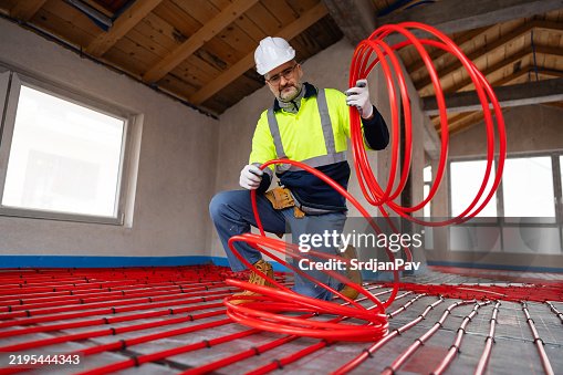 Construction Worker Installing Underfloor Heating with Red Pipe Coiling Construction Worker Installing Underfloor Heating with Red Pipe Coiling