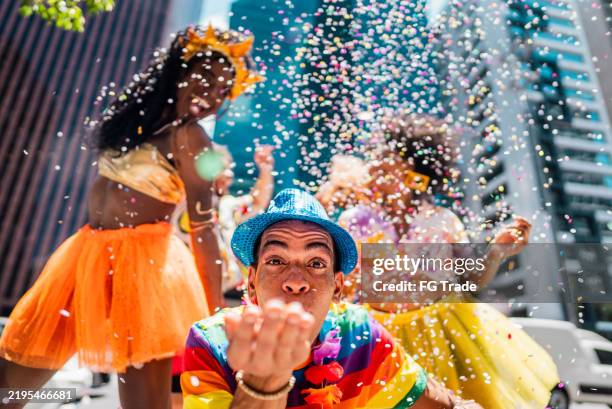 porträt eines mannes im mittleren erwachsenenalter, der konfetti bläst und sich mit freunden auf dem straßenkarneval amüsiert - karneval feier stock-fotos und bilder