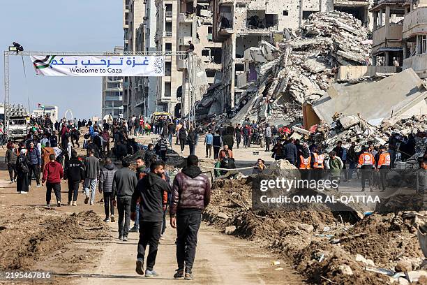 People gather by a banner welcoming people near the rubble of a collapsed building along Gaza's coastal al-Rashid Street for people to cross from the...