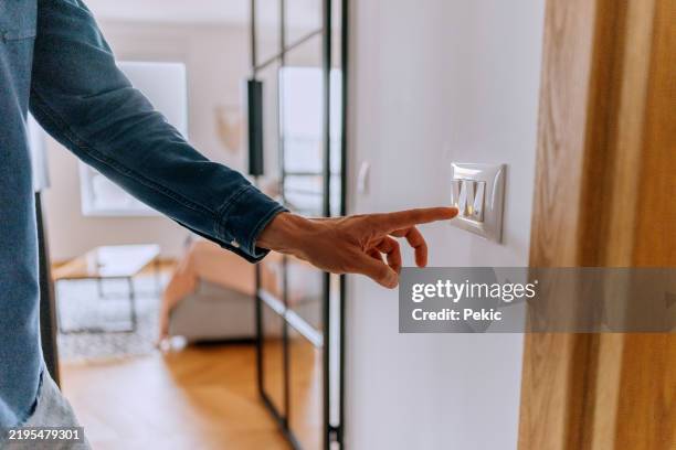 unrecognisable man turning on or off light switch at home - light switch stock pictures, royalty-free photos & images