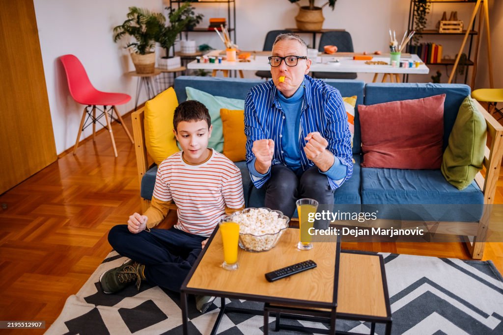 Father and his teenager son watching game together at home in living room and waiting for their favorite team to score