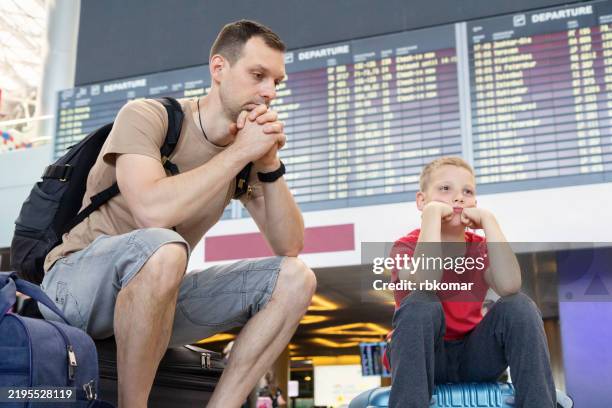 delayed flight status worries duo at terminal. young boy in red copies dad's concerned pose while monitoring digital board - cancellation stock pictures, royalty-free photos & images