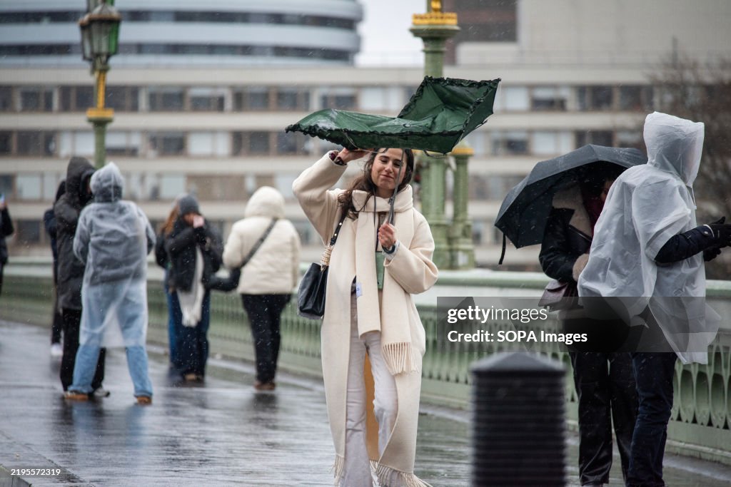 A pedestrian struggles with her umbrella due the strong...