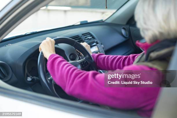 senior woman driving a car, holding the steering wheel - rijbewijs stockfoto's en -beelden