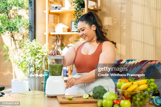 smiling woman overweight prepares a healthy smoothie in a bright home setting - plant based diet stock pictures, royalty-free photos & images