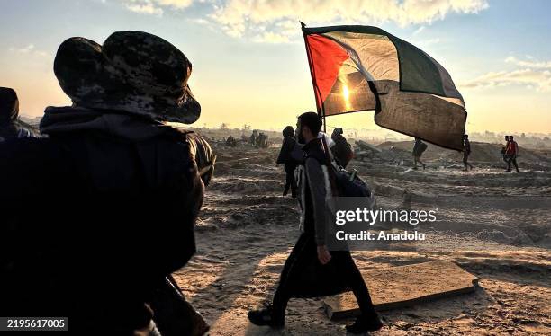 Man, carrying a Palestinian flag, walks as tens of thousands of Palestinians, displaced by Israel forces, return their houses through Al-Rashid...