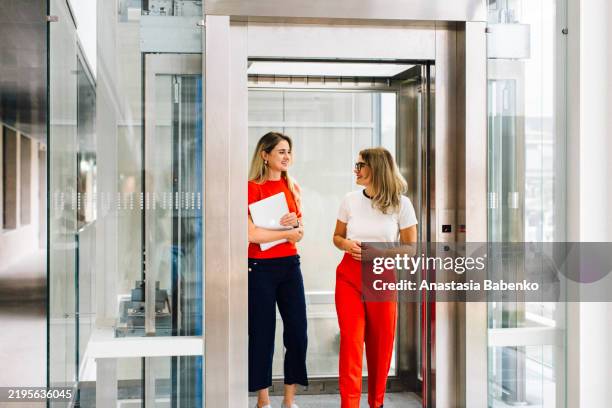 two young women having a professional conversation in elevator - two people in elevator stock pictures, royalty-free photos & images