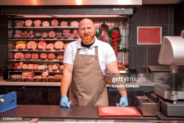 a handsome redhead male butcher during his daily duties serving in the shop - butcher stock pictures, royalty-free photos & images
