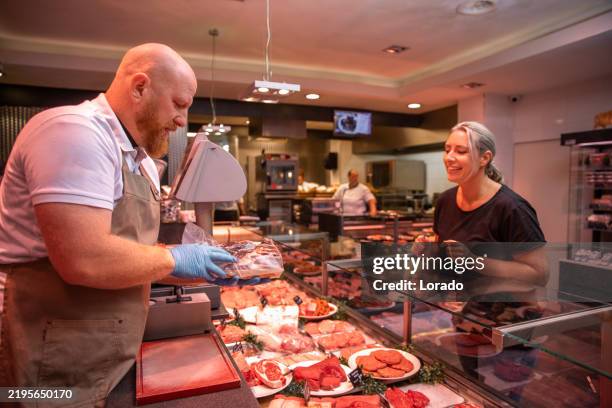 a handsome redhead male butcher serving a customer during his daily duties serving in the shop - butcher stock pictures, royalty-free photos & images
