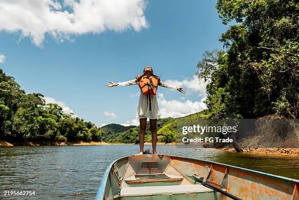 young woman standing at the edge of a boat with arms outstretched outdoors - amazonegebied stockfoto's en -beelden