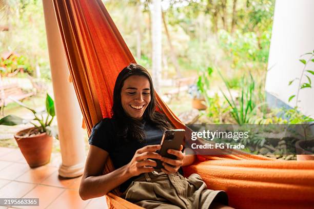 mujer joven usando el teléfono móvil en la hamaca al aire libre - hamaca fotografías e imágenes de stock